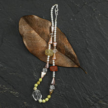 Stylish beaded necklace with pearls, gemstones on brown leaf and dark stone background