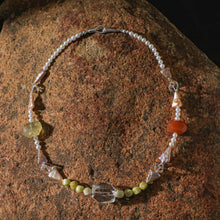 Artisan beaded necklace featuring pearls, yellow, red, and clear gemstones on rustic stone background