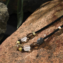 Beaded necklace with black, clear, smoky, and earthy stone beads on a textured brown rock