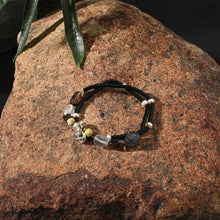 Beaded bracelet with black, clear, yellow, and white beads on a rough brown rock with green leaves