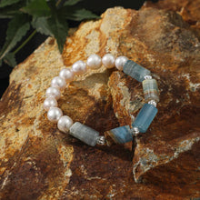 Pearl and blue gemstone bracelet displayed on textured rustic rock with green leaf