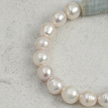 Close-up of a white freshwater pearl necklace with irregular round pearls on a light grey textured surface