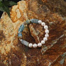 Pearl and aquamarine gemstone bracelet on rustic stone surface with green leaf