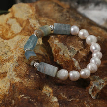 Bracelet featuring blue aquamarine stones and white pearls on a textured brown rock surface