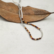 Beaded necklace with white, grey, and multicolored stones featuring silver tube detail on dried leaf