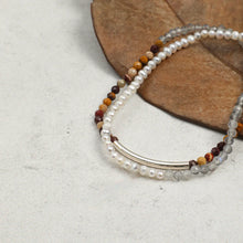 Two beaded bracelets with pearls, multicolor stones, and silver tube on gray and brown background