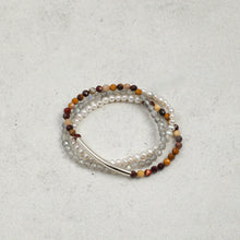 Three layered beaded bracelets with pearls, brown and orange stones, and silver tube on gray background