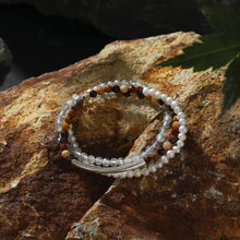 Stacked beaded bracelets with pearls and multicolor stones on textured rustic rock