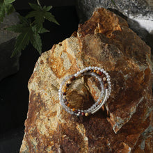 Three beaded bracelets with pearls and stones on rustic textured rock with a green leaf nearby