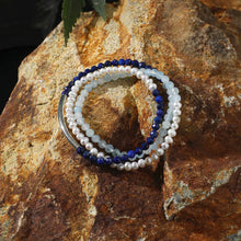 Triple-strand beaded bracelet with blue lapis, aquamarine, and white pearls on textured rock