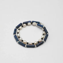 Double-strand bracelet with blue cylindrical beads, white pearls, black and silver round beads on white background