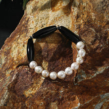 Elegant bracelet with white pearls and black oval beads on textured rust-colored rock