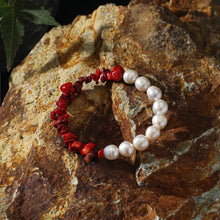 Red coral and white pearl bead bracelet on textured brown rock with green leaf