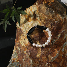 Black and white pearl beaded bracelet on textured natural rock with green leaf