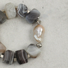 Close-up of a beaded bracelet with polished gray agate stones and a large irregular pearl on light background