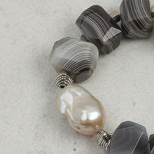 Close-up of a bracelet featuring large baroque pearl and faceted agate beads with silver spacers on grey surface