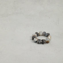 Chunky beaded bracelet with gray and white stones and a single large pearl on gray surface