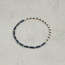 Delicate bracelet with blue cylindrical beads, white pearls, and small black beads on gray surface