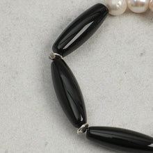 Close-up of black glossy elongated beads and white pearls on a textured gray surface
