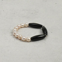 Elegant bracelet featuring irregular white pearls and elongated black beads on gray background