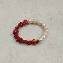 Bracelet featuring white pearls and red coral stones on a light grey surface