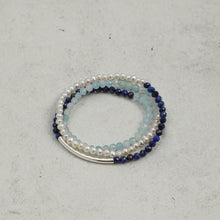 Stack of three beaded bracelets with pearls, aquamarine, and dark blue stones on gray surface