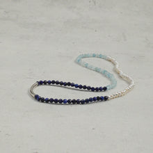 Delicate necklace with dark blue, light blue beads and white pearls on gray surface