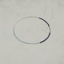 Delicate beaded necklace with pearl, light blue, and dark blue stones on gray background