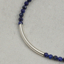 Close-up of faceted dark blue gemstone beads and curved silver tube on necklace