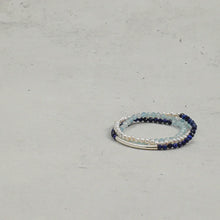 Stack of three beaded bracelets with pearls, blue and light blue stones on a gray surface