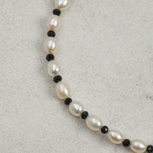 Close-up of a pearl necklace with alternating black beads on a neutral background