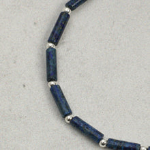 Close-up of blue cylindrical beads with small silver round spacers on a gray textured background