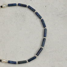 Close-up of a necklace featuring blue cylindrical beads, silver round spacers, and a single pearl on a gray background