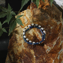 Pearl and lapis lazuli bracelet on textured brown rock with green leaves overhead