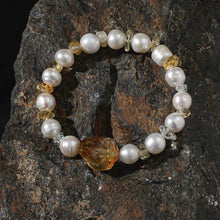Elegant bracelet with round white pearls and amber gemstones on a textured dark rock surface