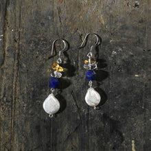 Handcrafted dangle earrings with pearl, blue, clear, and amber beads on rustic dark wooden surface