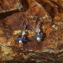 Handmade earrings with blue stone, clear quartz, and pearl on textured rustic rock background