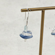 Handmade dangle earring with blue stone, clear glass bead, and silver hook on brass display