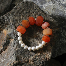 Bracelet with irregular orange carnelian stones and white pearls on dark textured rocks