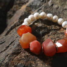 Close-up of a beaded bracelet with irregular white pearls and polished orange-red stones on rough rock