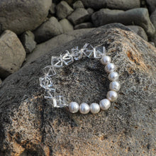 Elegant bracelet with white pearls and clear geometric beads on a textured rock surface
