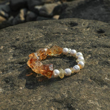 Bracelet with amber stones and white pearls on textured stone surface in natural sunlight