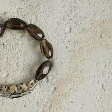 Close-up of bracelet with smoky brown beads, spotted stone beads, and silver chain on textured stone surface