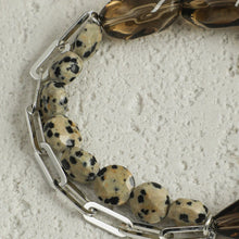 Close-up of dalmatian jasper beads and silver chain links on textured light surface