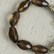 Close-up of polished smoky quartz beads on textured gray surface, part of beaded bracelet