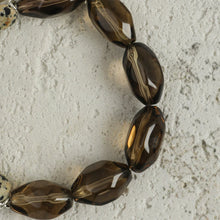Close-up of glossy faceted dark brown beads on textured gray surface