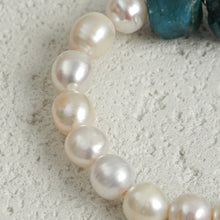 Close-up of a pearl and turquoise gemstone necklace on textured white surface
