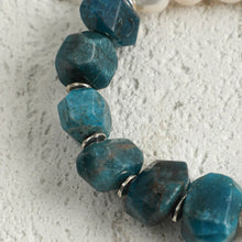 Close-up of a blue rough gemstone beaded bracelet with silver spacer beads on a textured gray background