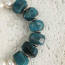 Close-up of blue faceted stones and white pearl beads on textured light surface jewelry