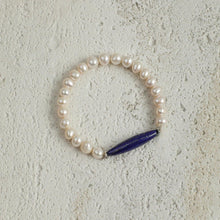 Elegant pearl bracelet with oval blue lapis lazuli centerpiece on textured stone background